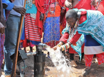 An image of a woman feeling water from a pump with her hands.