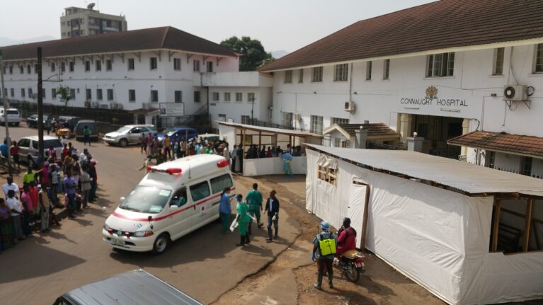 An ambulance outside of a hospital with outdoor tents for treatment of infectious disease.