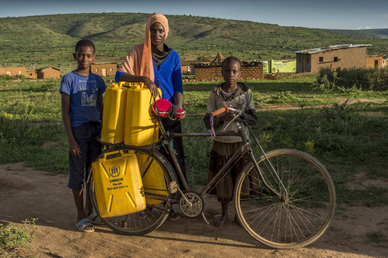 Siblings come back from a water collecting point pushing towards their house, a bicycle loaded with filled jerricans.