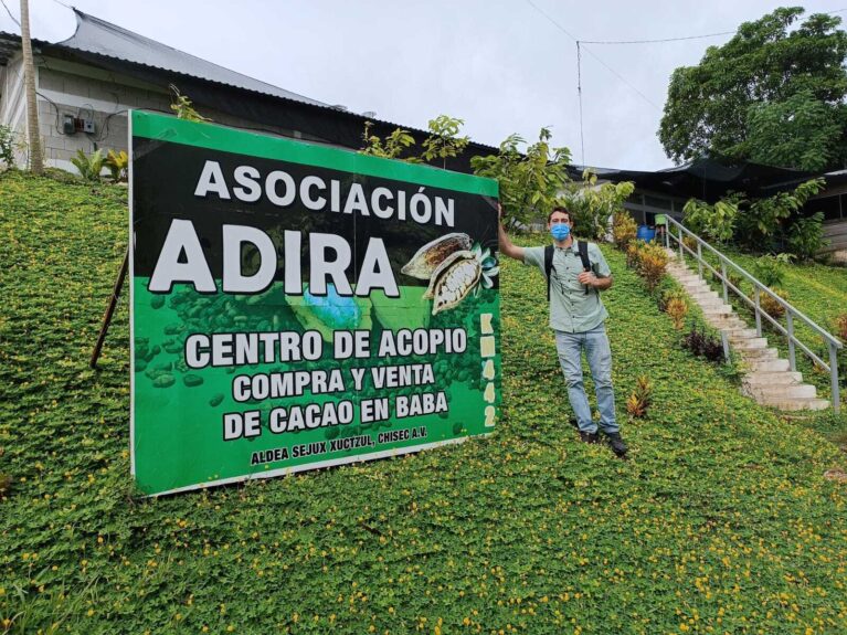 A volunteer standing next to a sign that highlights an engineering project for drying cardamom written in Spanish.